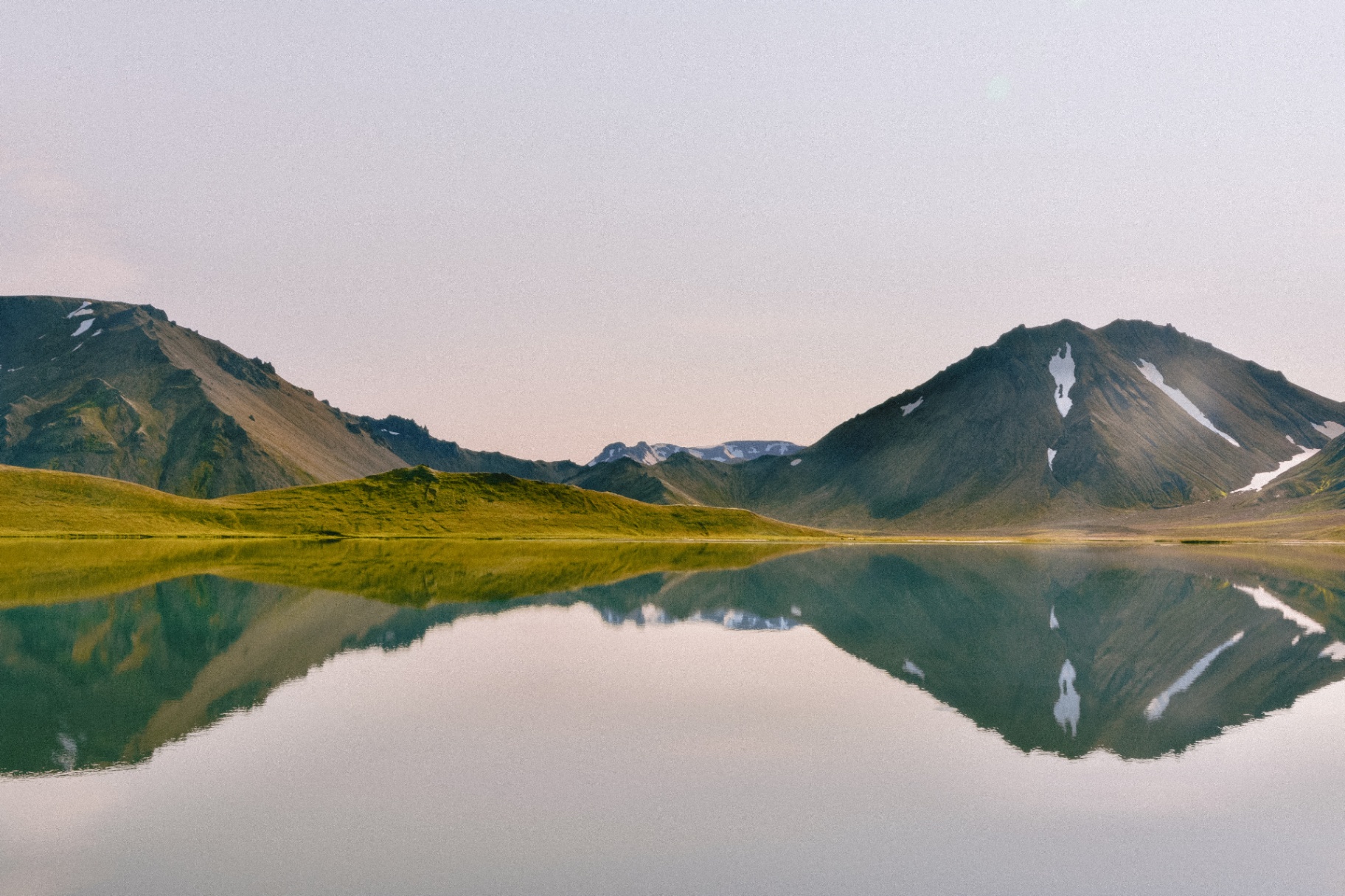 Deux pics aux formes douces se reflétant dans un lac d'altitude calme au crépuscule